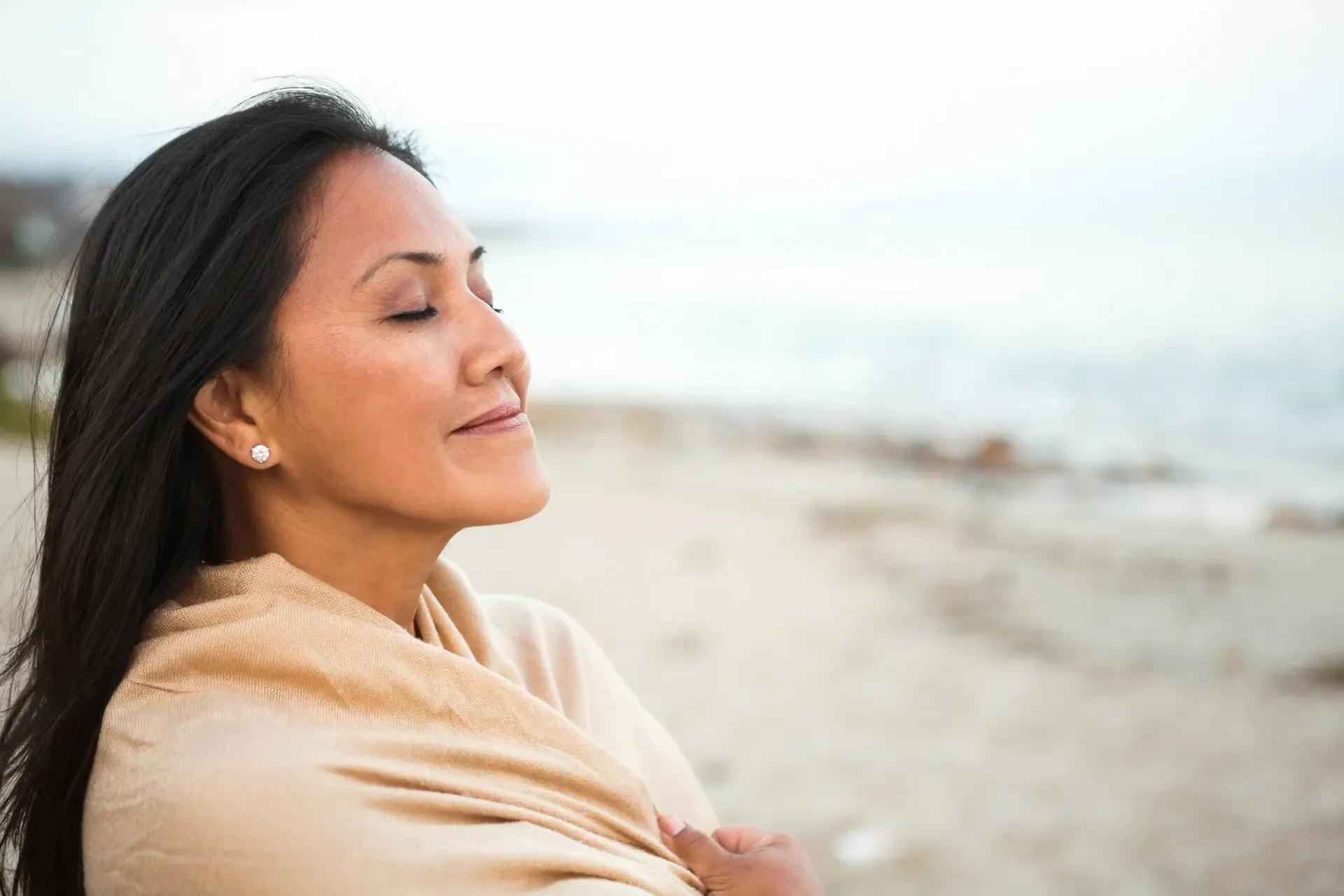 Woman standing on the beach, feeling rejuvenated as she enjoys the fresh air.
